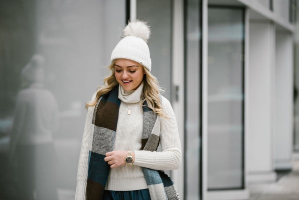 Bows & Sequins wearing a turtleneck sweater, a fur pom pom beanie, a checkered blanket scarf, and chambray wide leg pants.