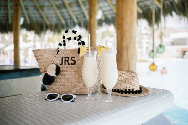 Kayu Designs monogrammed pom pom tote, pom-pom fedora, and black and white sunglasses at the swim-up bar at the Paradisus Los Cabos with pina coladas.