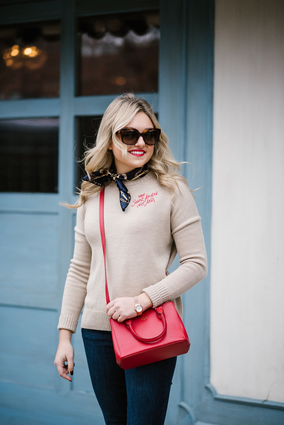 Fashion blogger Bows & Sequins styling a Parisian-inspired outfit... Maje sweater, Celine sunglasses, a silk neck scarf, and a red crossbody bag.