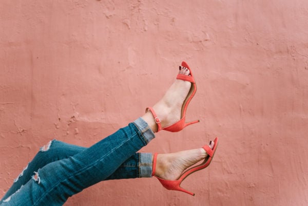 Fashion blogger Bows & Sequins wearing coral ankle strap sandals and cuffed skinny jeans against a pink wall in Chicago.