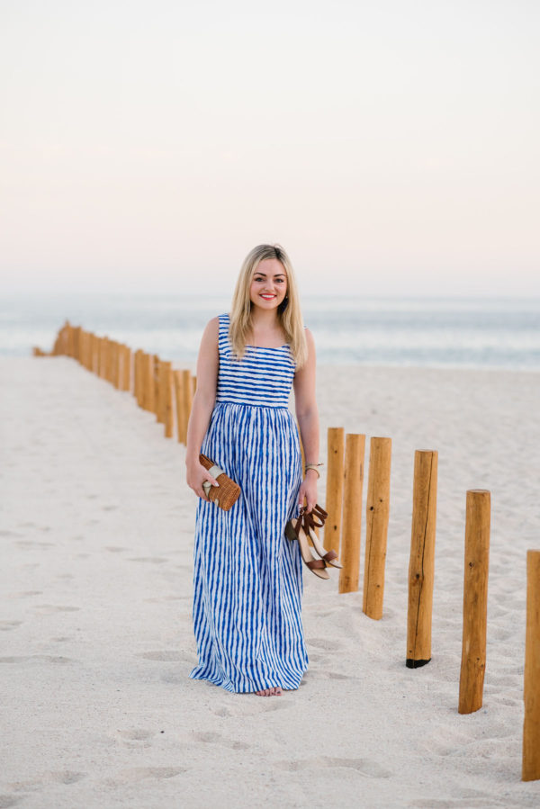 Bows & Sequins styling a blue striped maxi dress with a wicker clutch in Cabo San Lucas, Mexico.