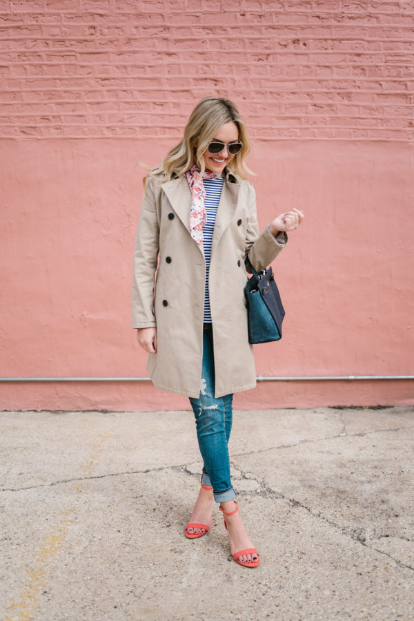 Jessica from Bows & Sequins wearing a tan trench coat with a navy Kate Spade bag, distressed denim, and coral heels.