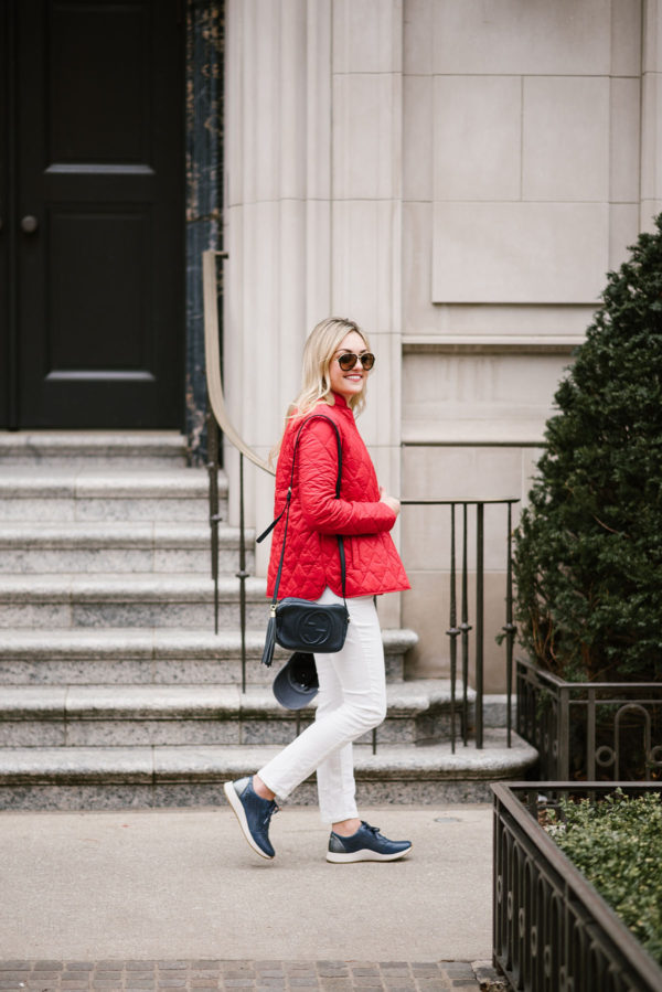 Bows & Sequins wearing a Barbour quilted red jacket, white jeans, a Gucci crossbody bag, and navy blue sneakers.