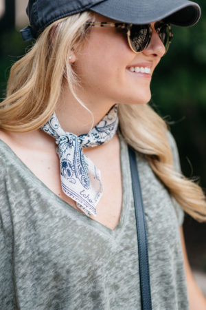Jessica of Bows & Sequins styling a printed bandana with a navy baseball cap, Illesteva sunglasses, and v-neck tee.