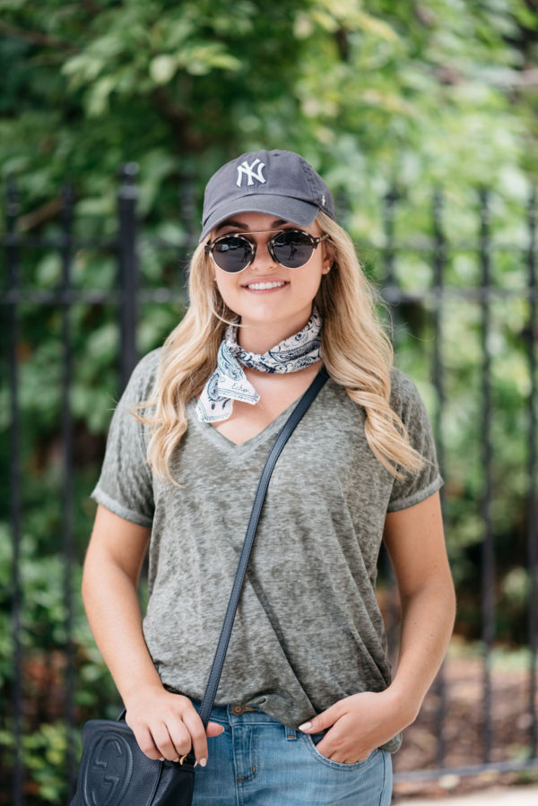 Travel blogger Bows & Sequins wearing a New York Yankees hat with a printed bandana and a crossbody bag at a park in Amsterdam.