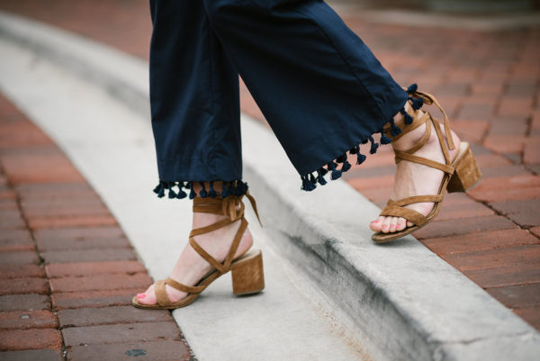 Bows & Sequins wearing navy blue tassel pants with tan lace-up suede sandals.