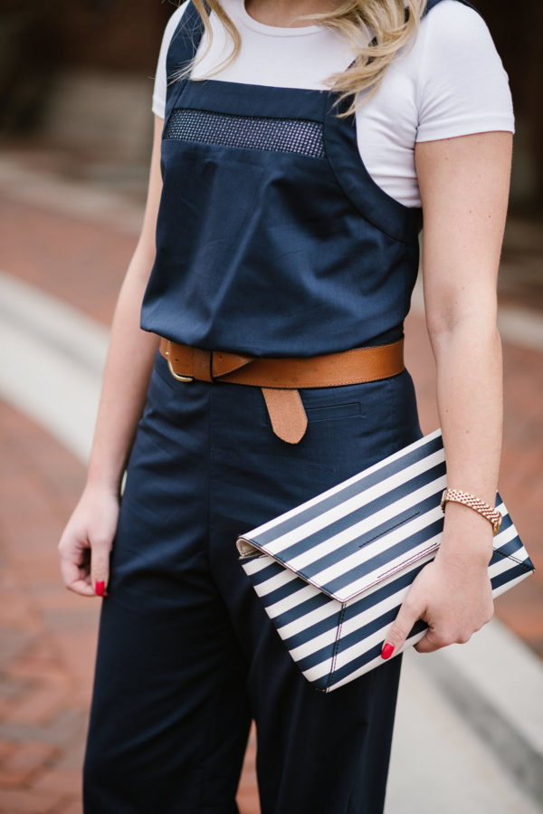 Bows & Sequins styling a leather belt with a navy blue jumpsuit and a striped envelope clutch.