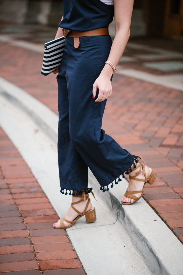 Bows & Sequins wearing a navy blue jumpsuit with a leather belt and lace-up sandals.