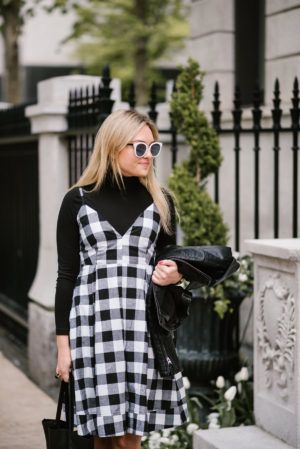 Fashion blogger Bows & Sequins wearing black and white sunglasses, a gingham dress, and black turtleneck top.