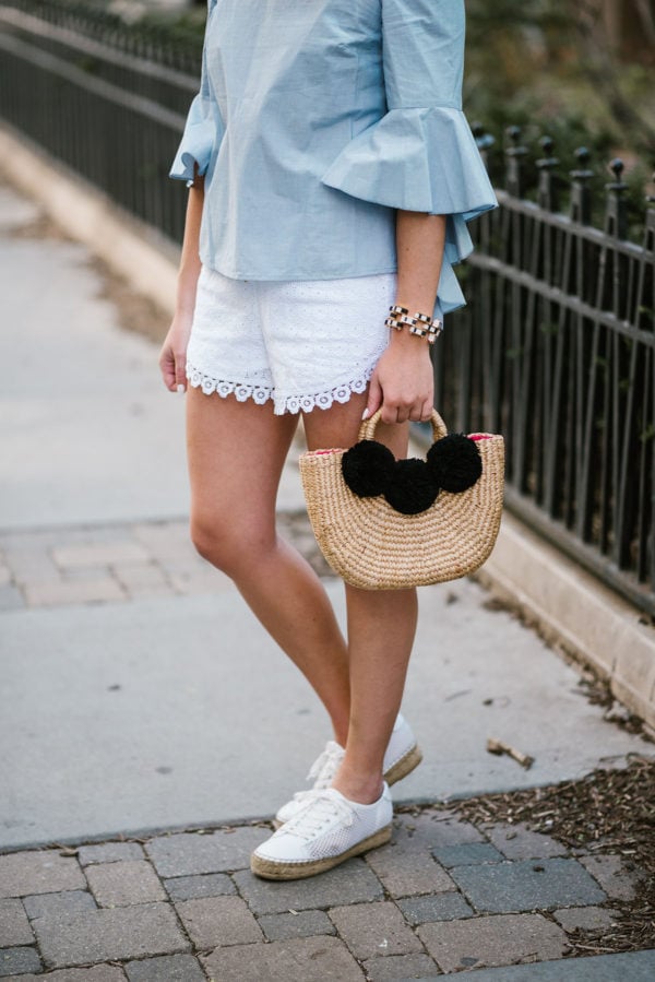 Bows & Sequins wearing a Kensie chambray top with white eyelet shorts, a JadeTribe pom pom basket bag, and Marc Fisher espadrilles.