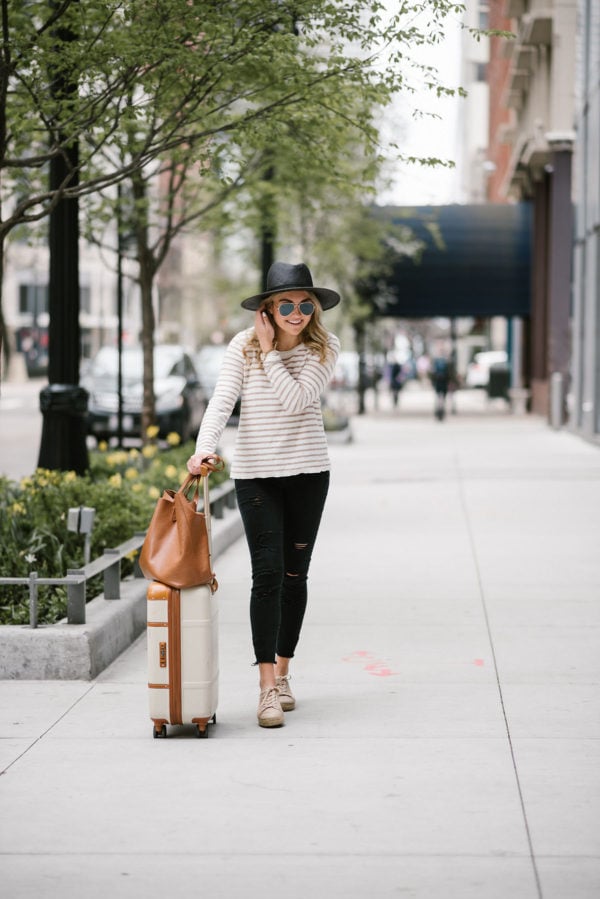 Bows & Sequins sharing her go-to travel outfit: straw hat, striped sweater, raw hem jeans, and espadrille sneakers.
