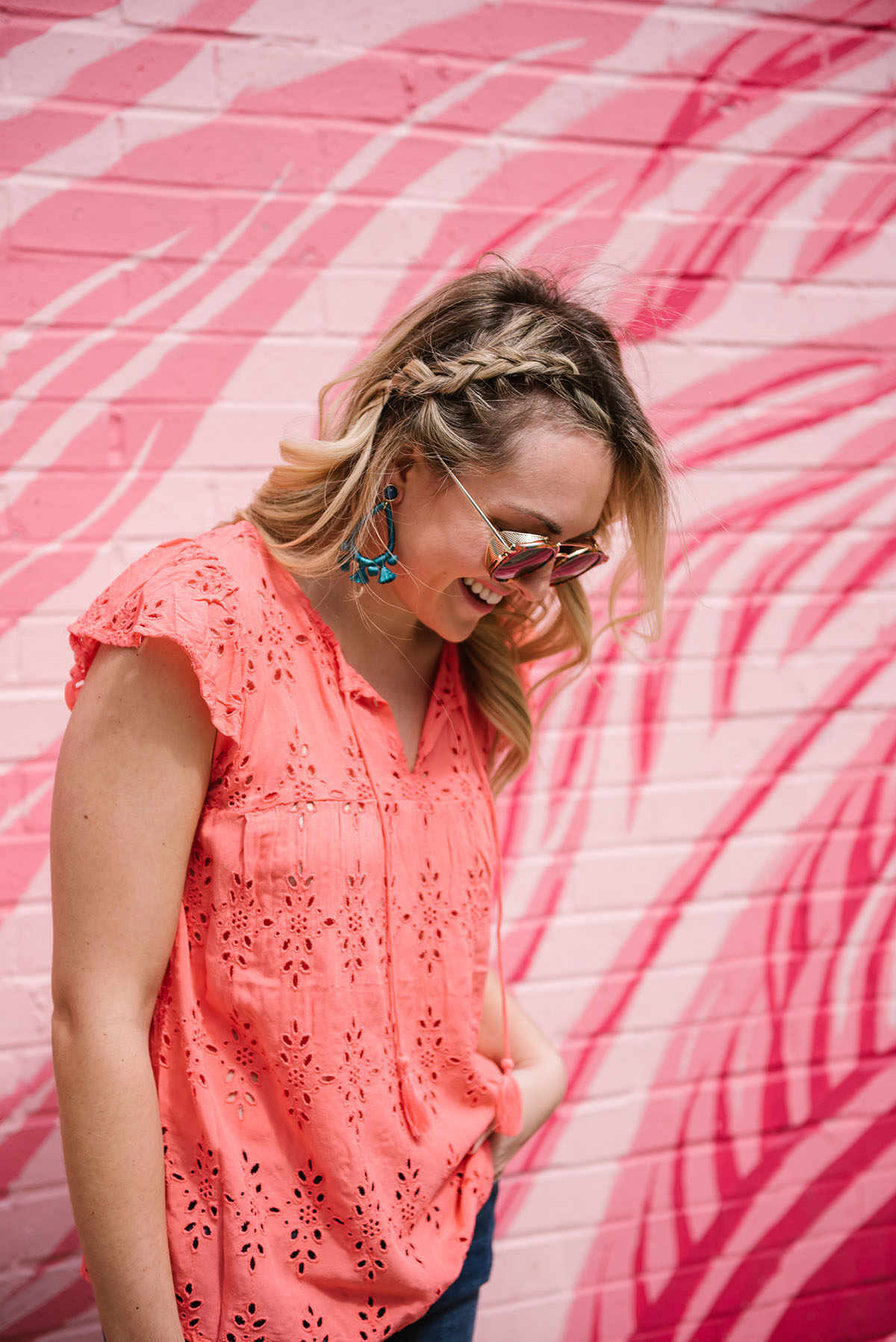 Bows & Sequins wearing a coral eyelet top, sunglasses from Hadid Eyewear, and BaubleBar statement earrings in front of the pink flamingo wall in Chicago