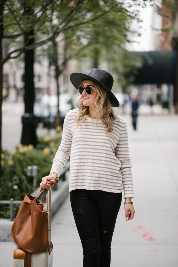 Chicago blogger Bows & Sequins wearing a black straw Janessa Leone hat with gold Ray-Ban aviators, a striped Kenzie sweater, and Old Navy jeans with a Cuyana leather tote for travel.
