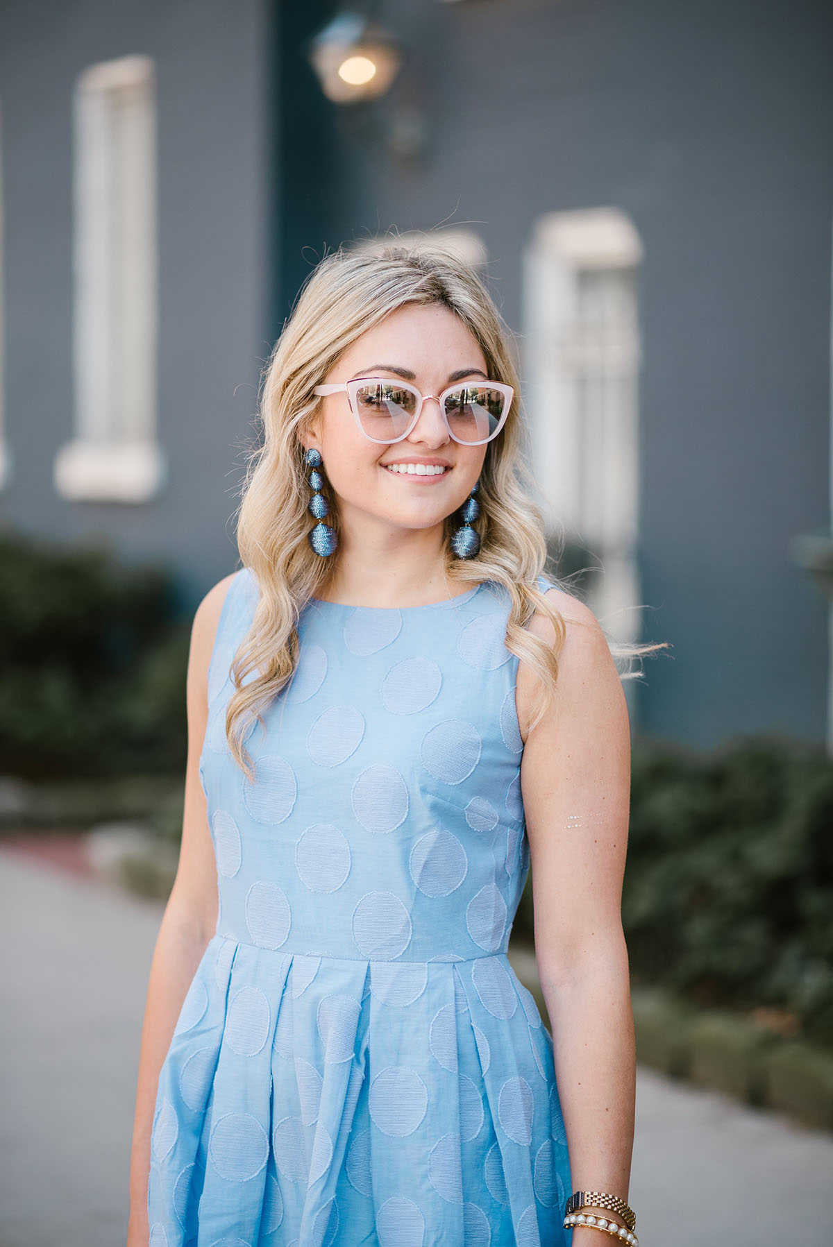 Jessica of Bows & Sequins in a hydrangea blue dress with blush pink sunglasses and Tuckernuck statement earrings.