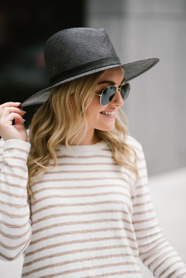 Jessica of Bows & Sequins styling a black Janessa Leone hat with a striped Kenzie sweater and gold Ray-Ban aviators.