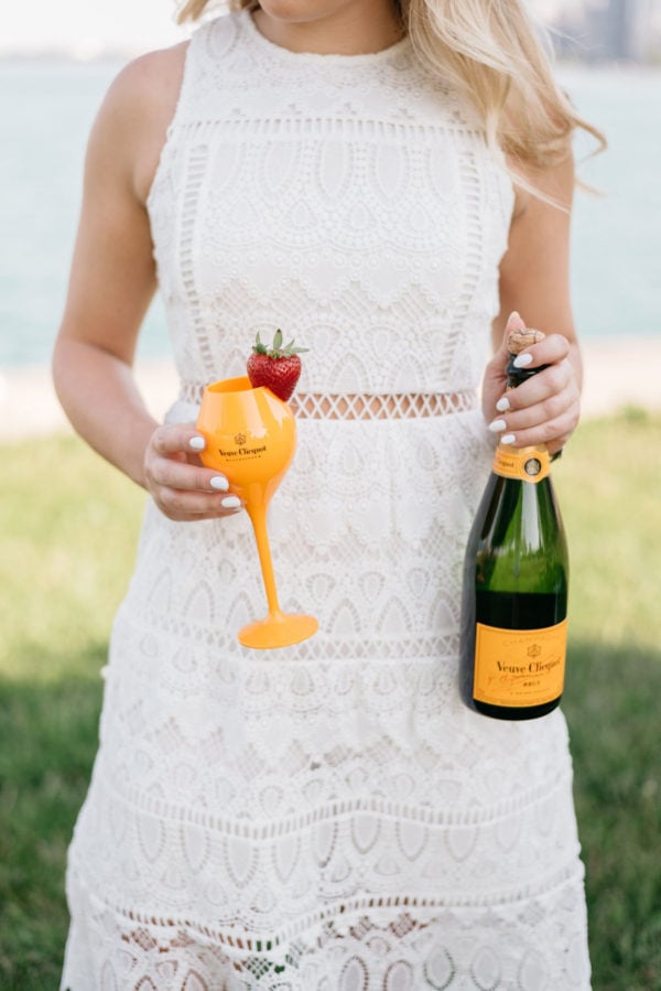 Bows & Sequins holding Veuve Clicquot champagne and wearing a white lace J.O.A. dress.
