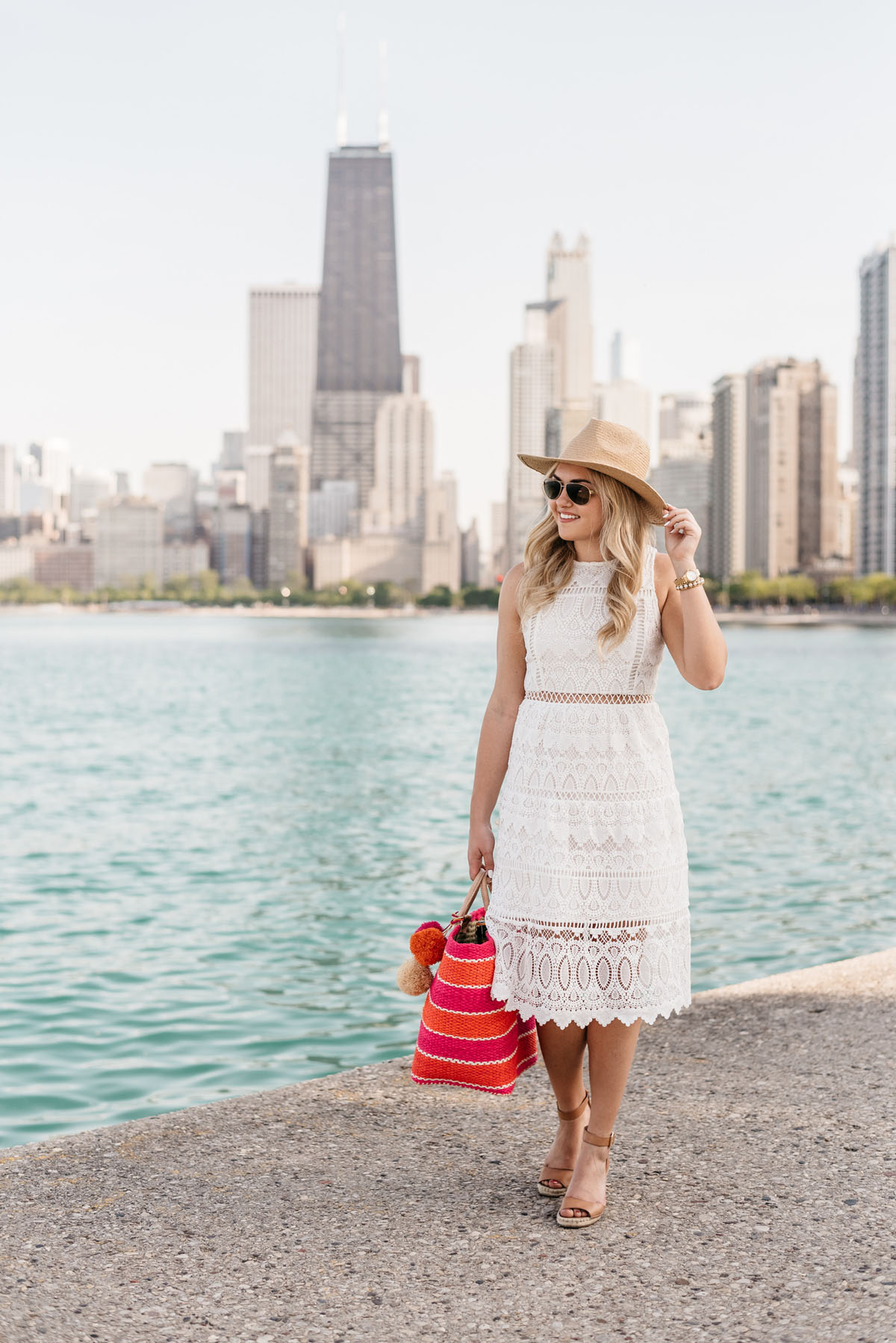Fashion blogger Bows & Sequins wearing a white lace J.O.A. dress, an Old Navy straw hat, and holding a striped Mar y Sol tote.