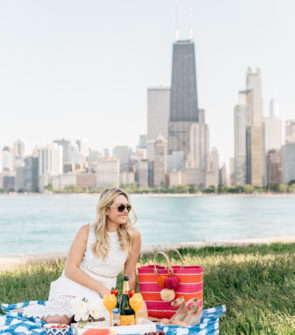 Chicago blogger Bows & Sequins wearing a J.O.A. lace dress with a Mar y Sol straw tote on a Crate & Barrel blue gingham blanket.