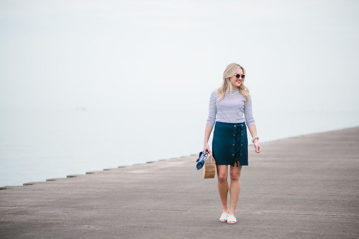 Fashion and style blogger Jessica Sturdy of Bows & Sequins wearing a three quarter sleeve tee and navy skirt with white slides and a bamboo bag.