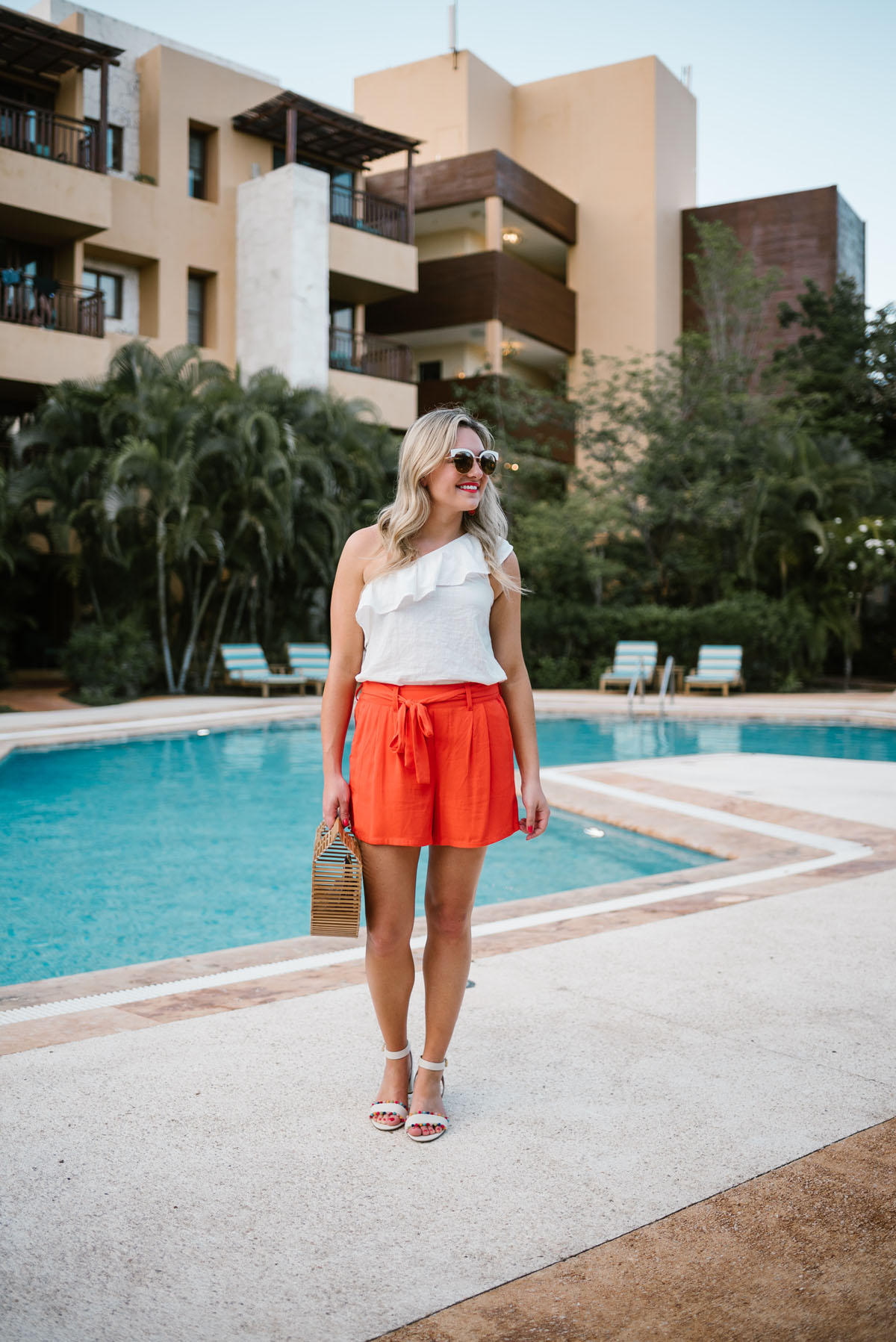 Travel writer Jessica Sturdy of Bows & Sequins wearing an Old Navy one-shoulder ruffle top with orange tie-waist shorts and J.Crew pom-pom sandals.