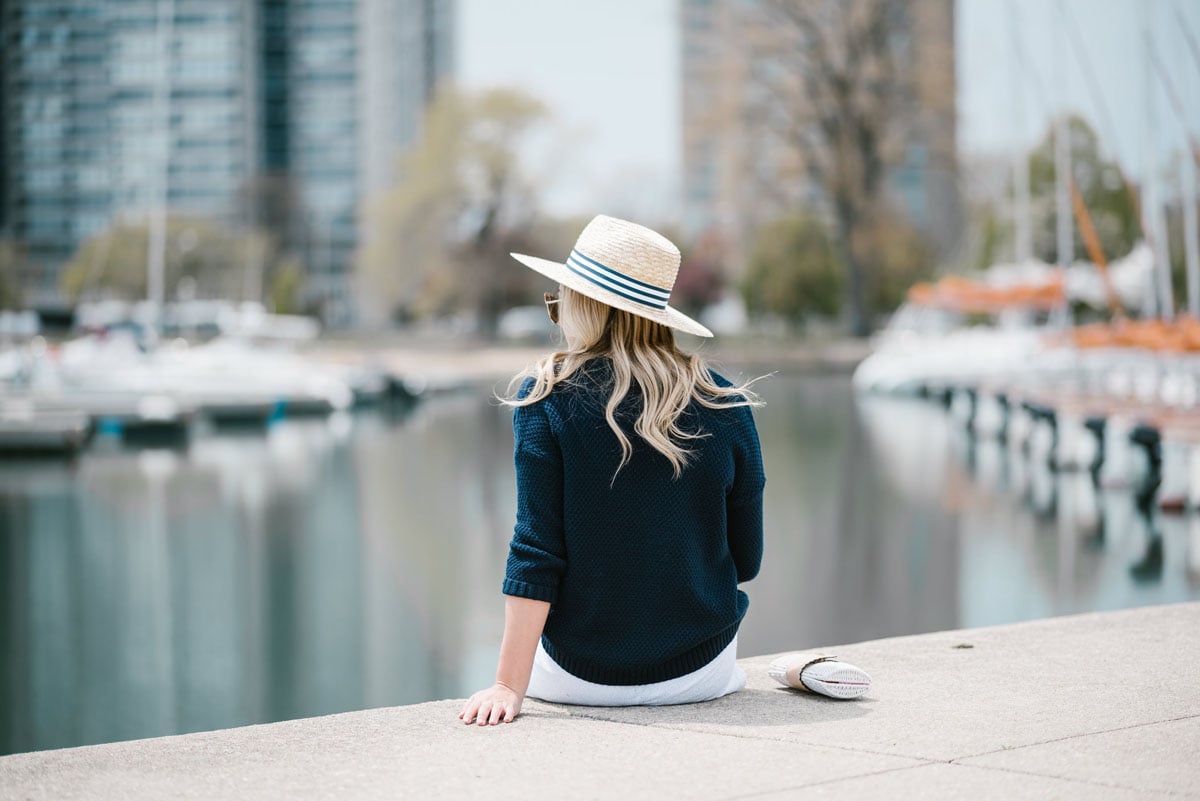 Chicago blogger Bows & Sequins wearing a straw hat with a striped band and a navy sweater.