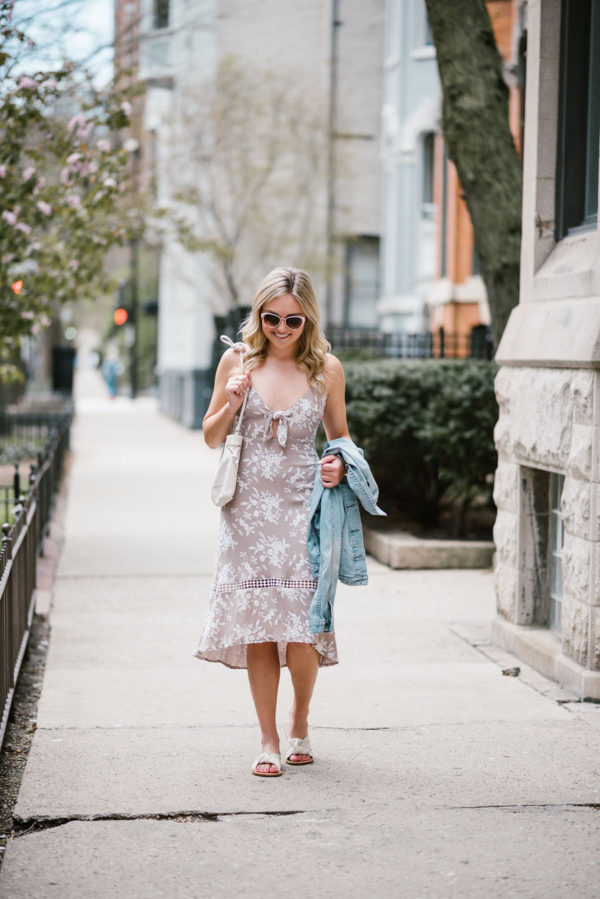 Jessica of Bows & Sequins wearing a floral tie-front dress with a Clare V Petit Henri bag, a Gap light denim jacket, white Soludos knotted slides, and Call It Spring sunglasses.