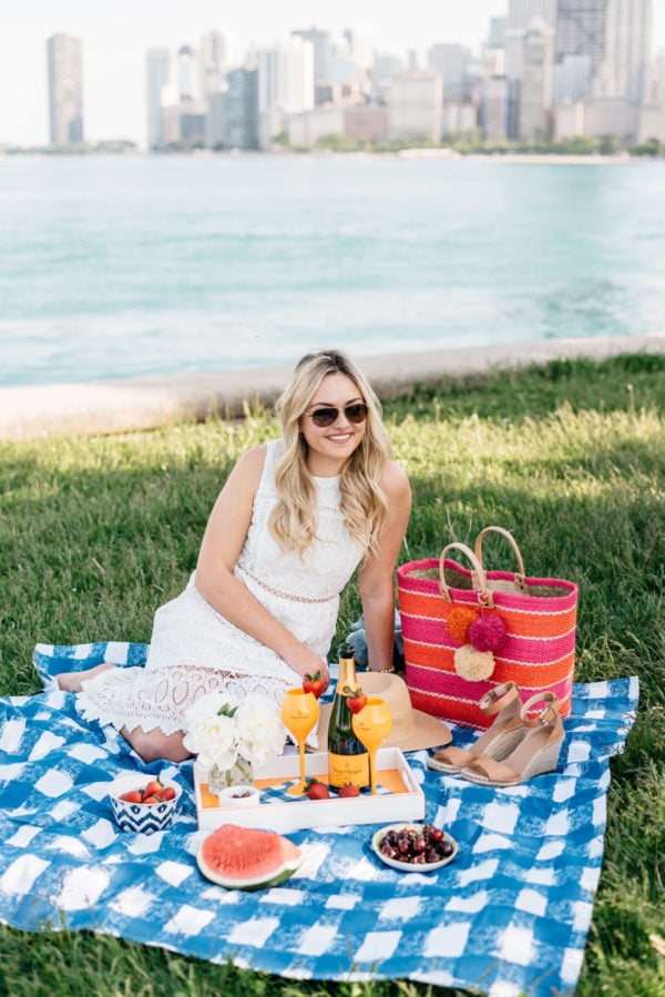 Chicago blogger Bows & Sequins wearing a white lace dress and a Mar y Sol striped tote on a gingham picnic blanket.