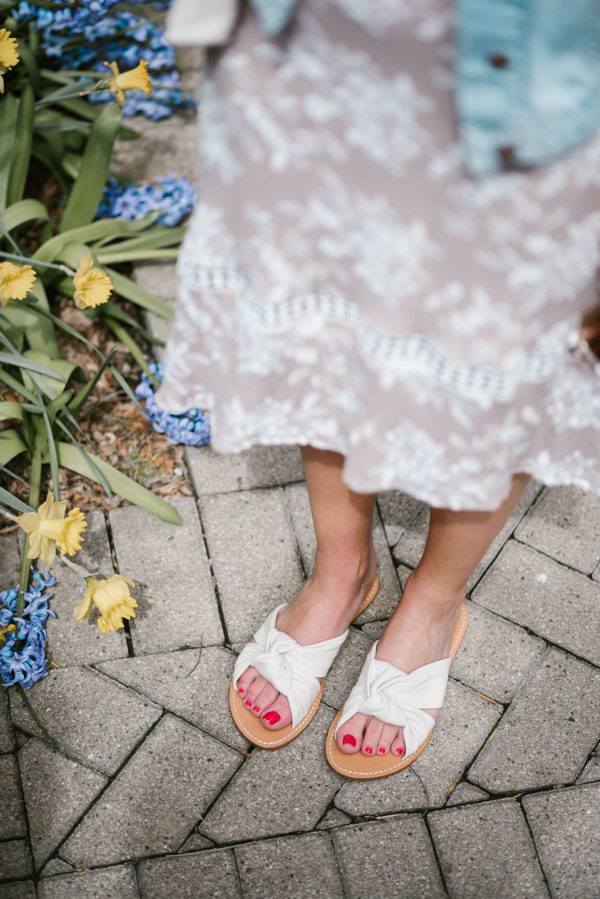 Bows & Sequins styling white Soludos knotted slides with a floral midi dress and light wash jean jacket.