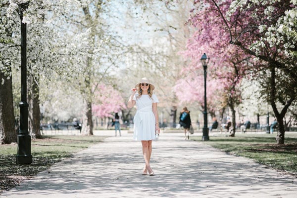 Bows & Sequins wearing a white fit and flare dress with a straw hat in Chicago during the springtime.