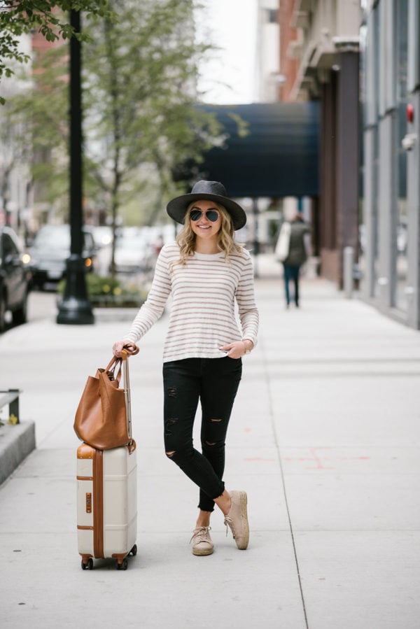 Fashion blogger Bows & Sequins wearing distressed black jeans with a striped sweater and straw hat for traveling.