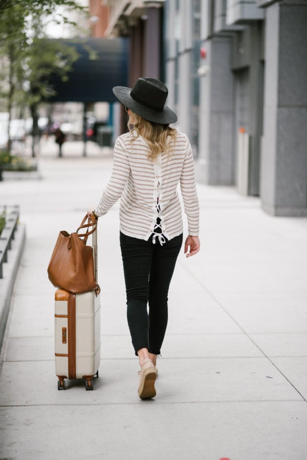 Lifestyle blogger Bows & Sequins sharing her top tips for traveling comfortably with a casual sweater, jeans, Brics bellagio suitcase and Cuyana leather tote.