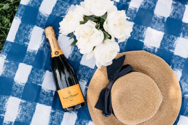 Tuckernuck straw hat with a navy hat on a Crate & Barrel blue gingham picnic blanket and Veuve Clicquot champagne.