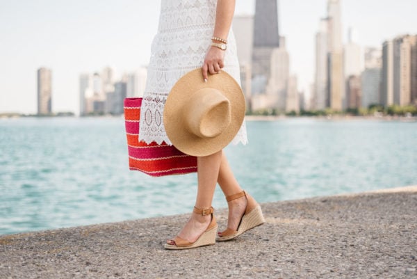 Fashion blogger Jessica Sturdy of Bows & Sequins wearing a J.O.A. lace dress and Vince Camuto espadrille wedges with a striped straw tote and an Old Navy hat.