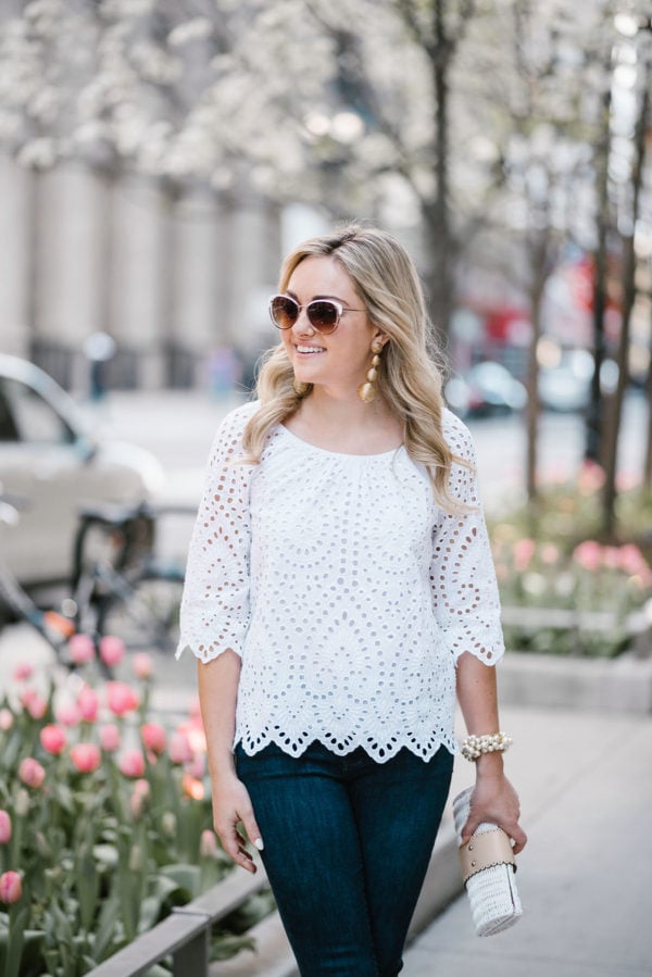 Bows & Sequins wearing a white Vineyard Vines eyelet top with Call It Spring white rim sunglasses, Tuckernuck gold statement earrings, and a wicker rattan clutch in downtown Chicago.