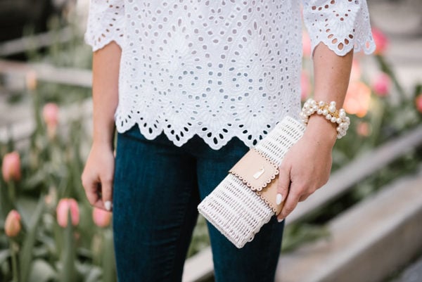 Fashion blogger Bows & Sequins holding a Vineyard Vines white wicker rattan clutch and wearing a Sweet & Spark pearl bracelet.