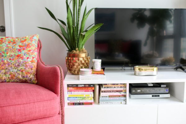 Bows & Sequins Chicago living room decor with a pink wingback chair and colorful printed throw pillow, snake plant, and stacked books.