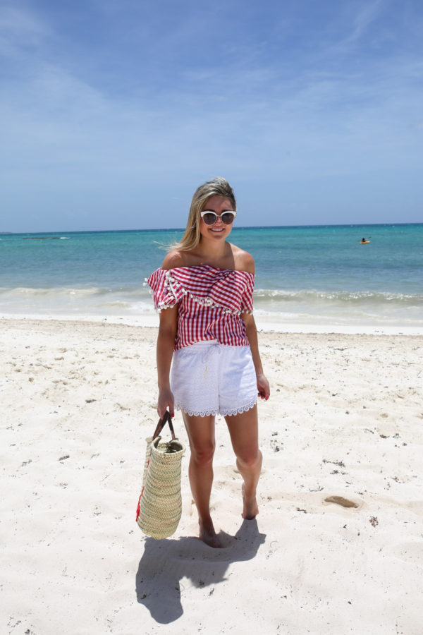 Travel blogger Bows & Sequins wearing an off the shoulder red gingham top with white shorts and a Bad and Boujee straw tote at the Fairmont Mayakoba in Mexico.
