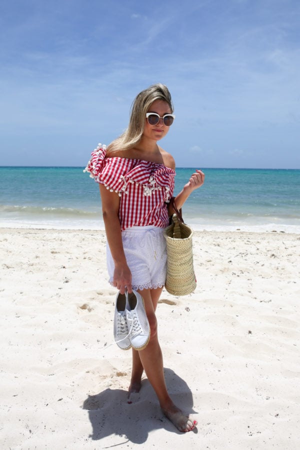 Bows & Sequins wearing a red gingham pom pom hem top with white shorts and a straw tote at the Fairmont Mayakoba resort in Mexico.
