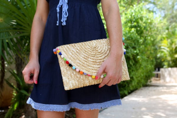 Bows & Sequins styling a navy Sail to Sable bathing suit cover up with a pom pom clutch at the Fairmont Mayakoba resort in Mexico.