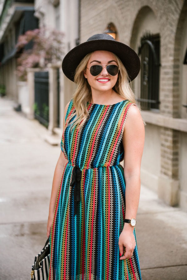 Bows & Sequins wearing a rainbow crochet dress with a black straw hat and aviators.