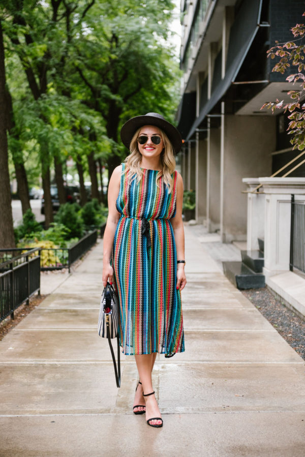 Travel writer Bows & Sequins wearing a rainbow striped Eva Franco dress from Anthropologie with a black straw hat and sandals.