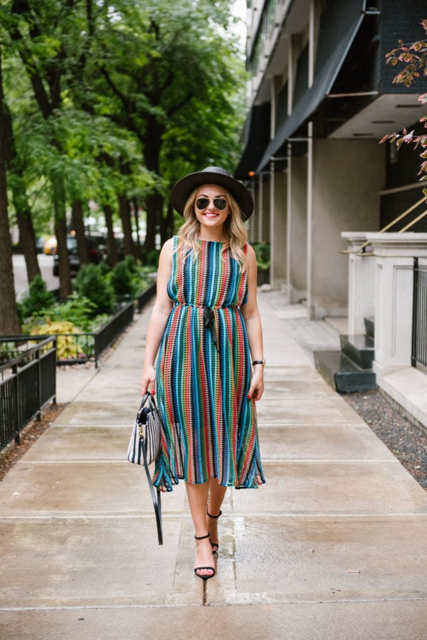 Bows & Sequins styling a rainbow striped midi dress with black sandals, aviators, and a black straw hat.