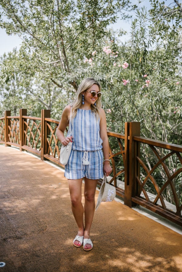 Fashion blogger Bows & Sequins wearing a blue and white Vineyard Vines romper with white Soludos knotted slides and a Clare V Petit Henri bucket bag.