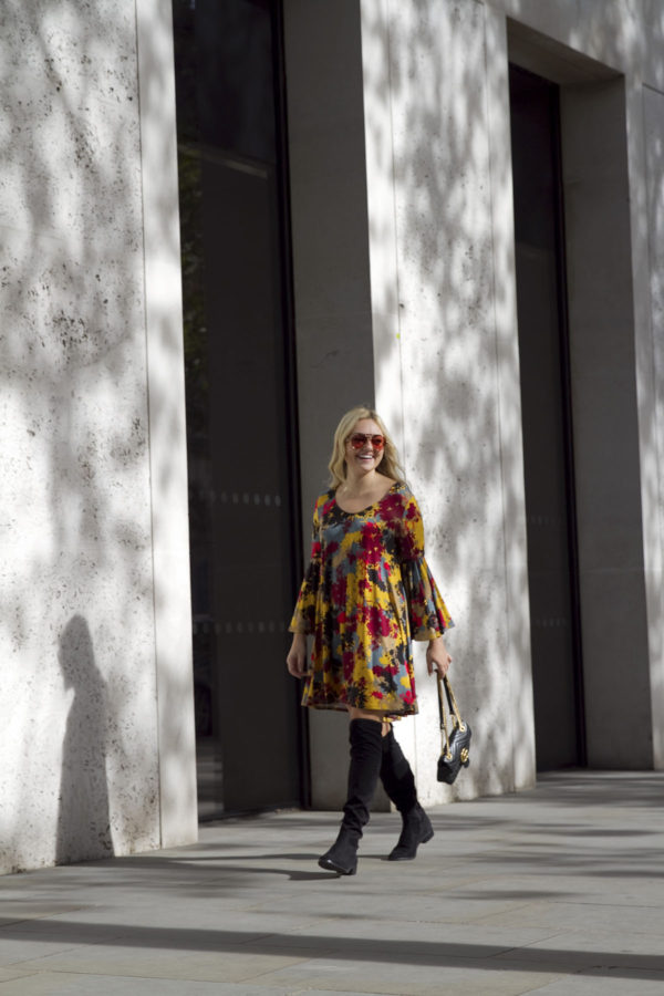 Travel writer Bows & Sequins wearing a printed floral bell sleeve dress with sunglasses and over the knee boots in London.