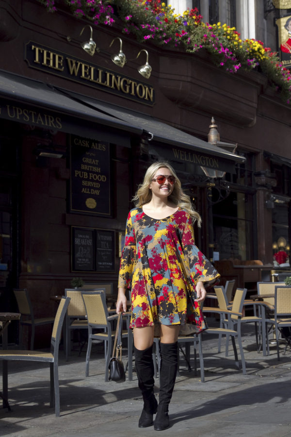 Fashion and lifestyle blogger Bows & Sequins outside The Wellington in London wearing a printed floral swing dress with flat over the knee boots and a Gucci bag.