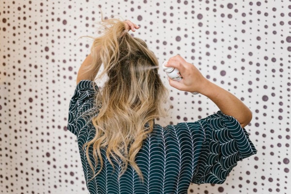 Blonde demonstrating how to use dry shampoo spray in her hair.