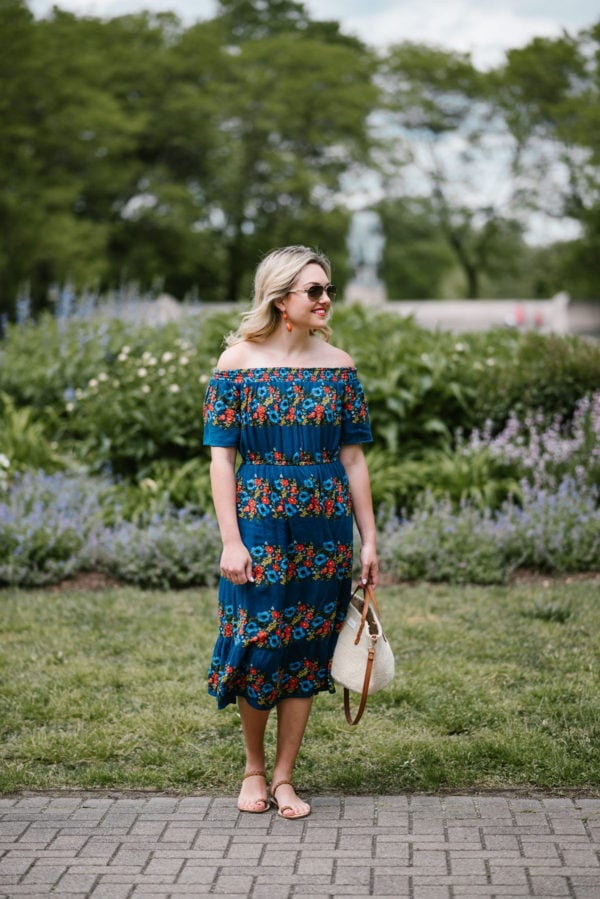 Chicago fashion blogger Bows & Sequins wearing an off the shoulder floral dress with a straw handbag, aviators, and strappy leather sandals.