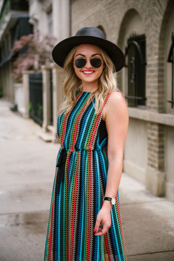 Bows & Sequins, a travel lifestyle blogger, wearing an Eva Franco rainbow striped dress from Anthropologie with a black straw hat for summer.