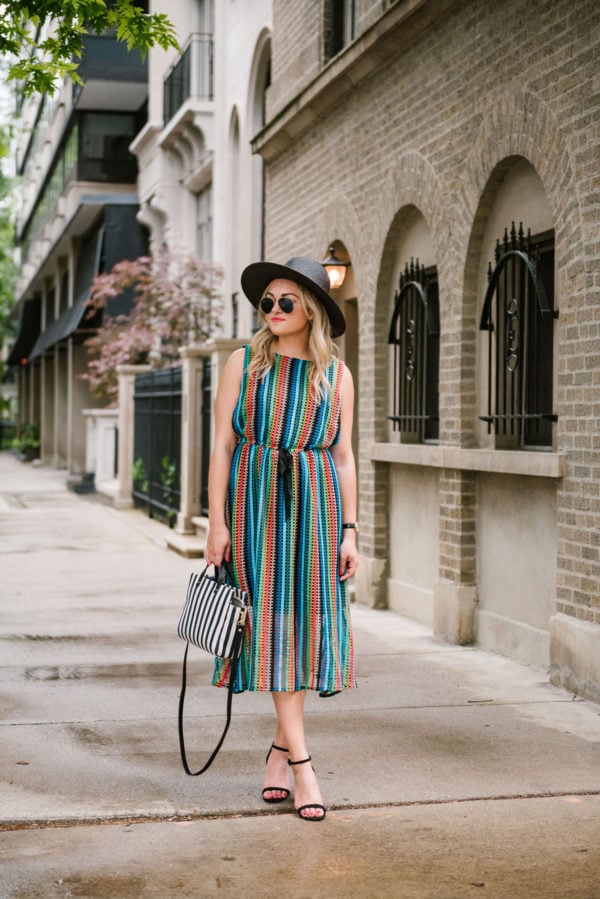 Travel blogger Bows & Sequins wearing a black straw hat, rainbow striped Eva Franco midi dress from Anthropologie, and black sandals.
