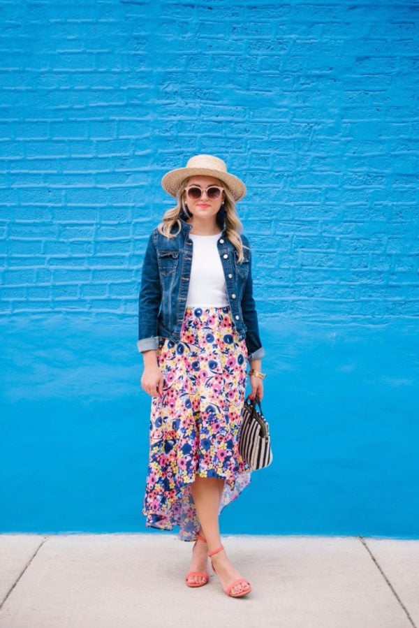 Fashion-focused lifestyle blogger Bows & Sequins wearing a Hutch floral high-low dress from Anthropologie with a denim jacket, Nordstrom sunglasses, and a L Space straw hat.